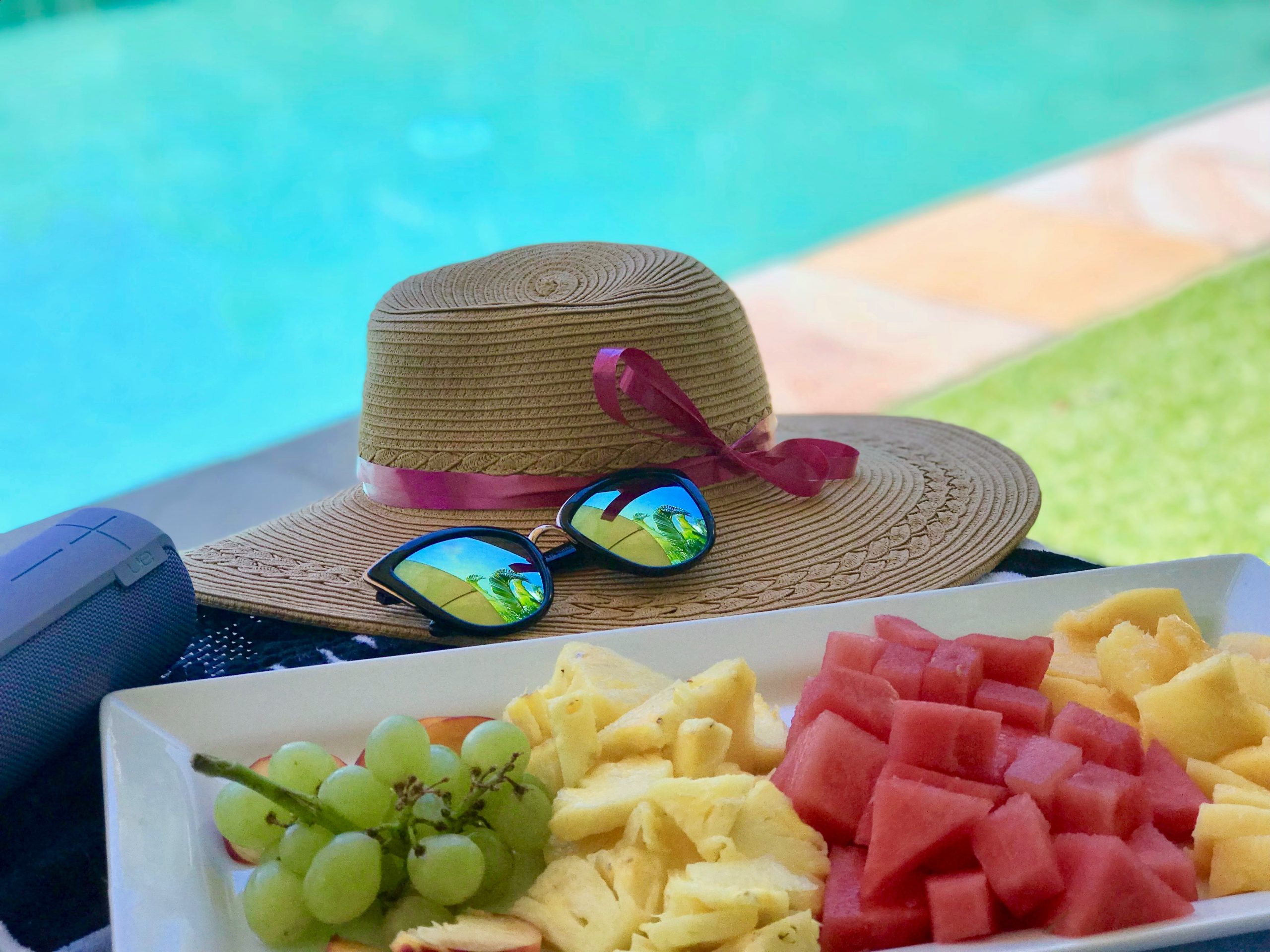 rodajas de fruta en bandeja blanca junto a gafas de sol y sombrero de paja